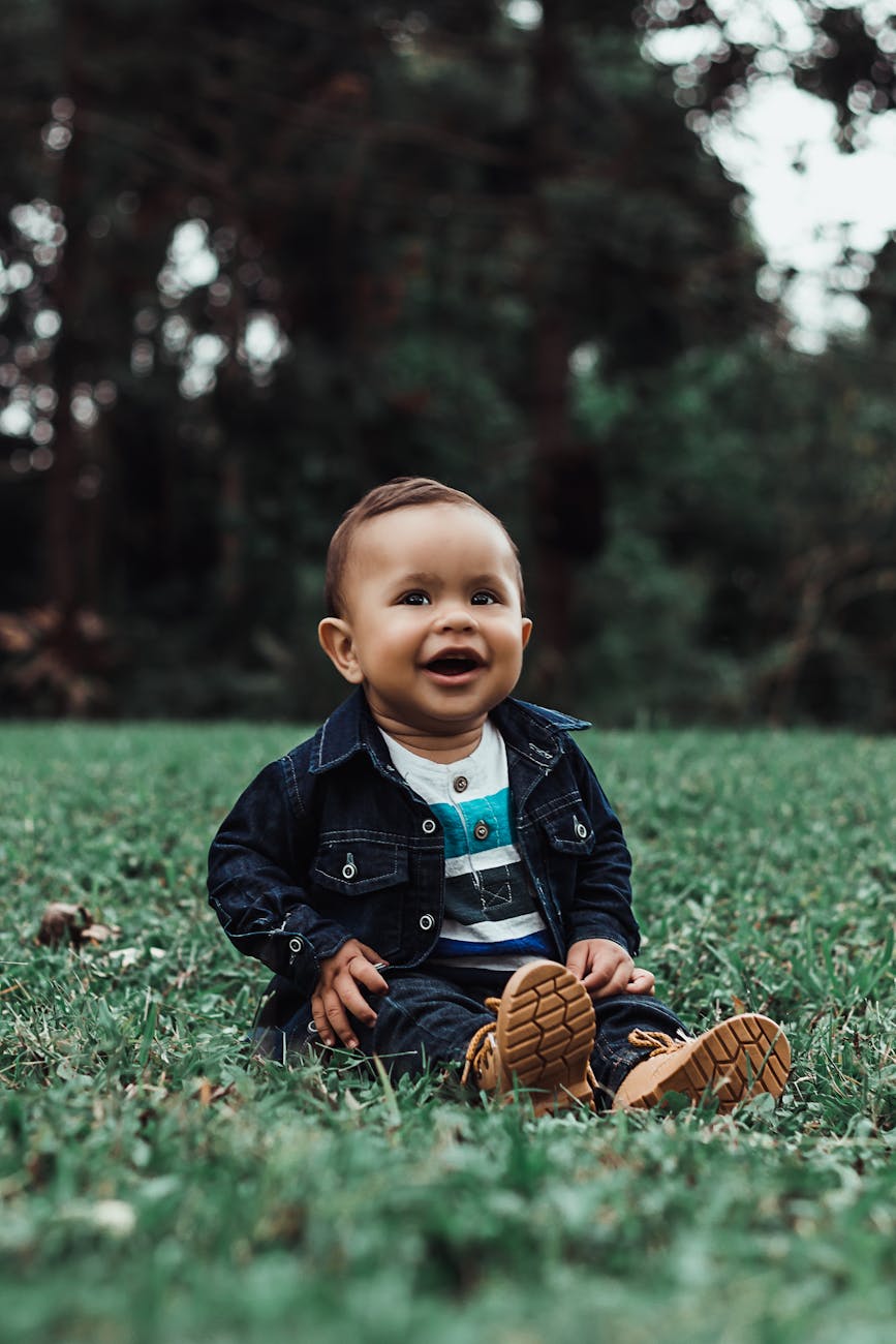 photo of smiling baby boy in denim outfit sitting on grass