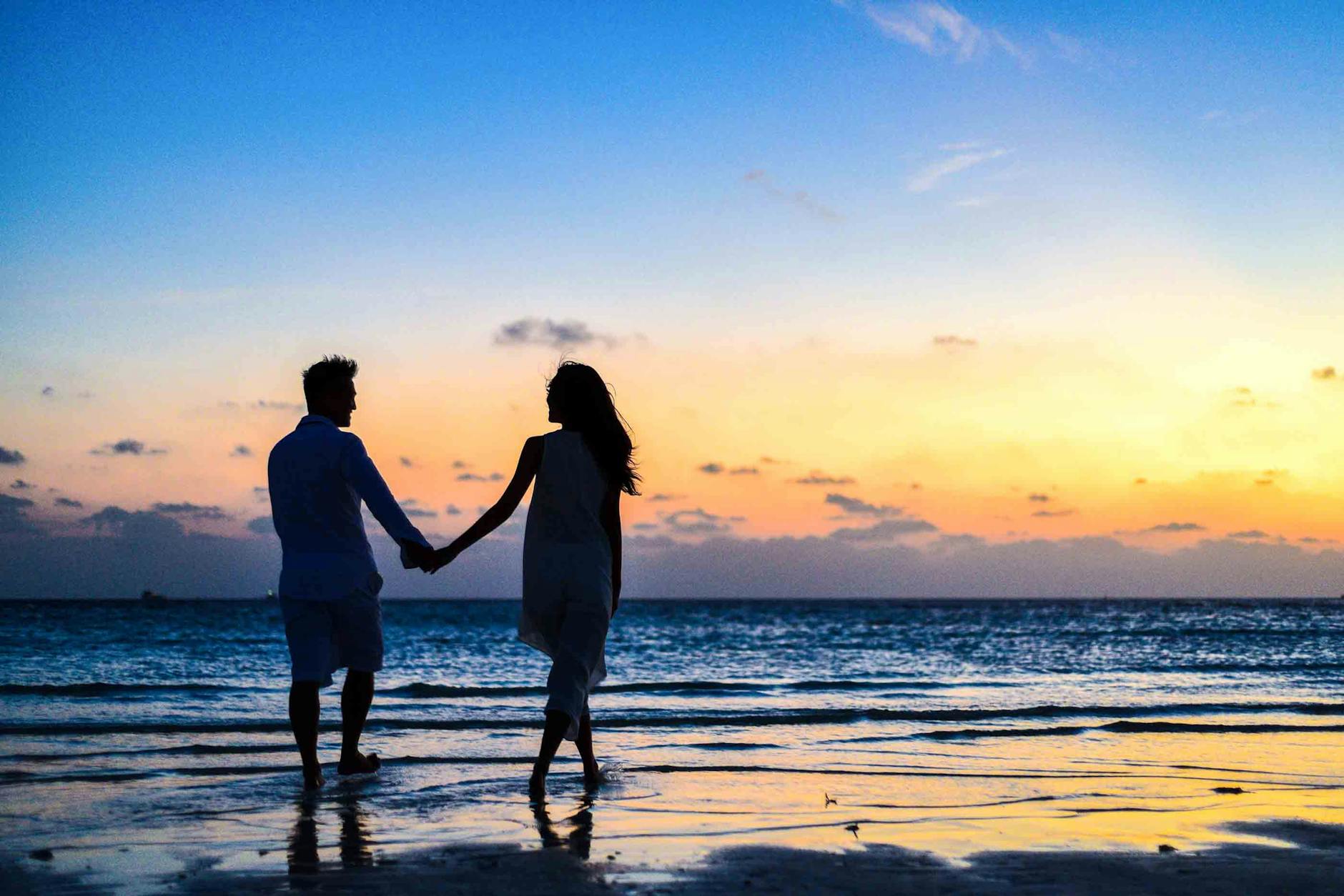 homem e mulher de mãos dadas andando na praia ao por do sol