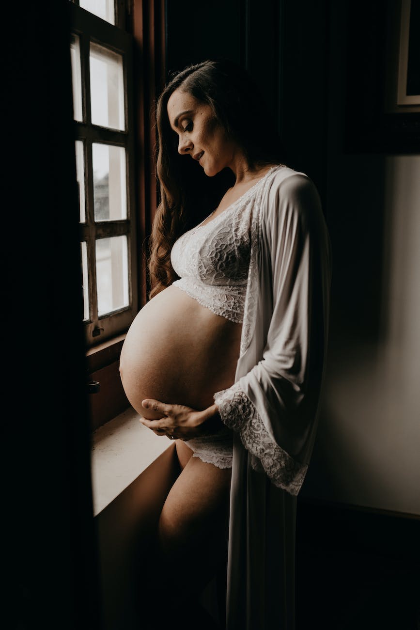 mulher grávida vestindo um cardigã ao lado da janela