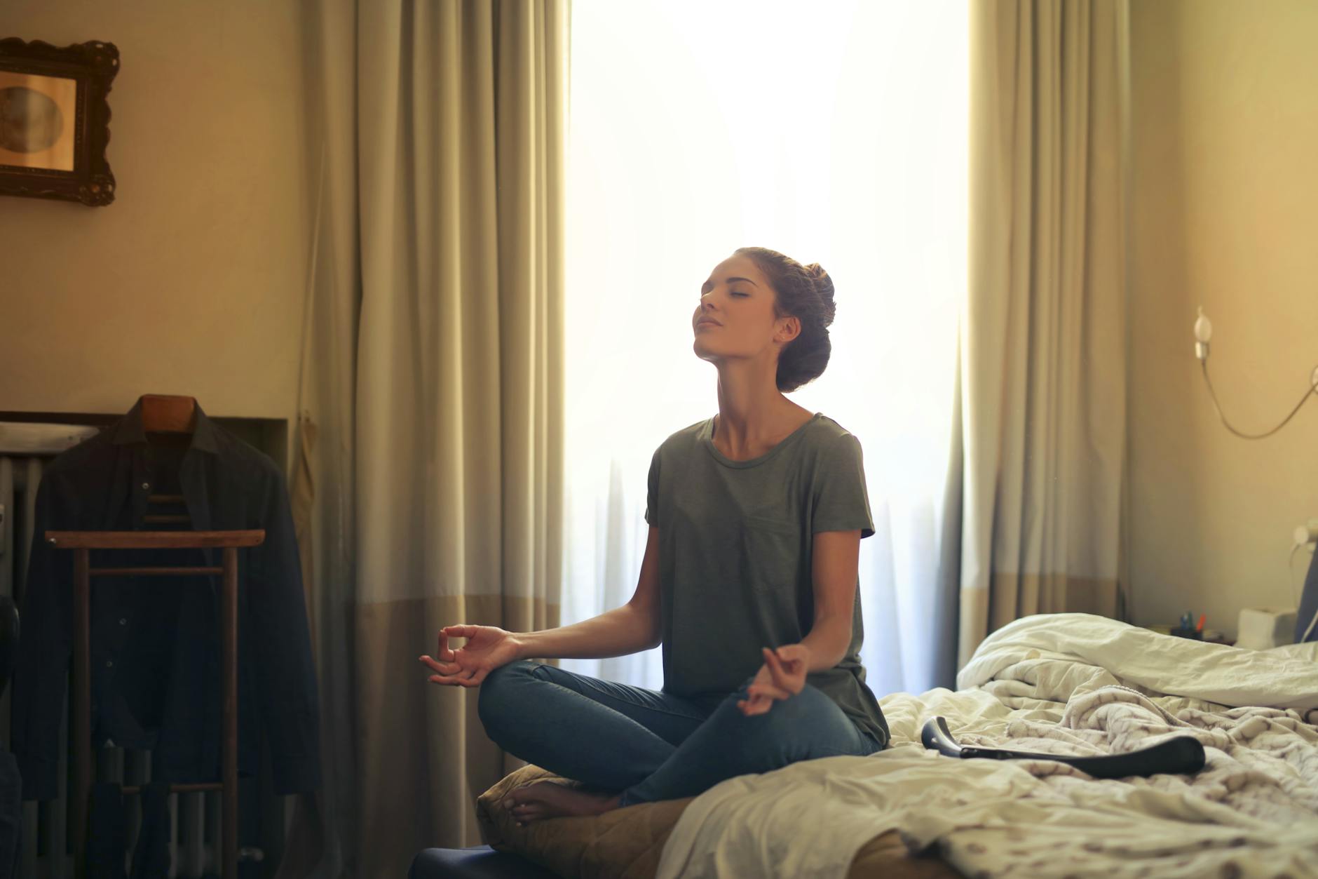 mulher meditando no quarto em cima da cama