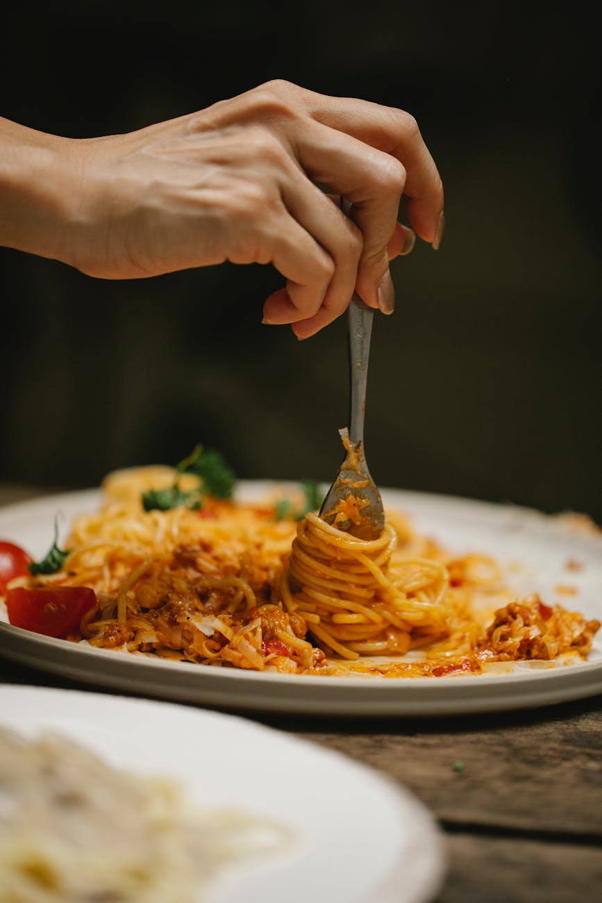 mulher irreconhecível com garfo saboreando uma deliciosa massa à bolonhesa