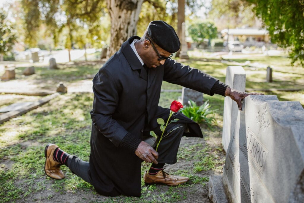 a grieving man kneeling on a grave with red flower