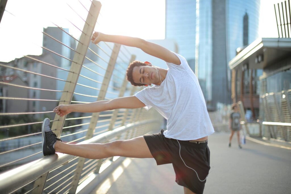 young slender ethnic sportsman in earbuds warming up and listening to music with pleasure on street in city