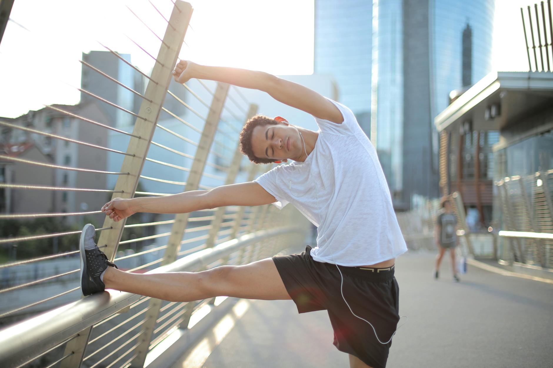 young slender ethnic sportsman in earbuds warming up and listening to music with pleasure on street in city