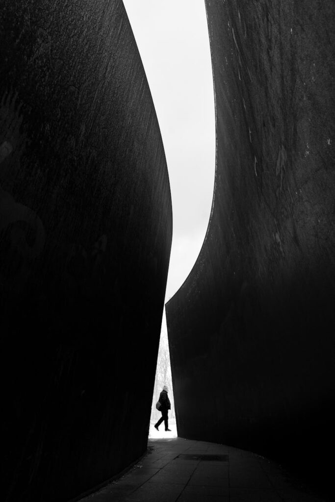 silhouette of a person walking between large concrete walls of a modern building in city