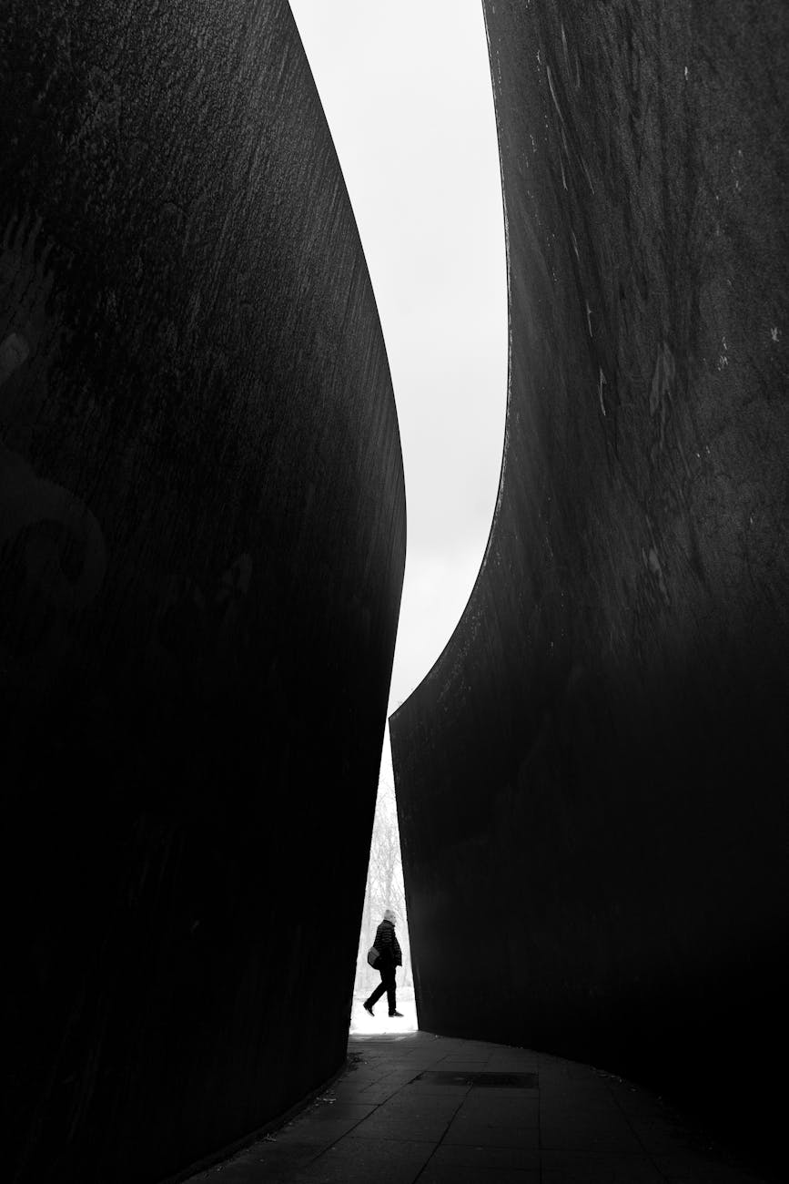 silhouette of a person walking between large concrete walls of a modern building in city