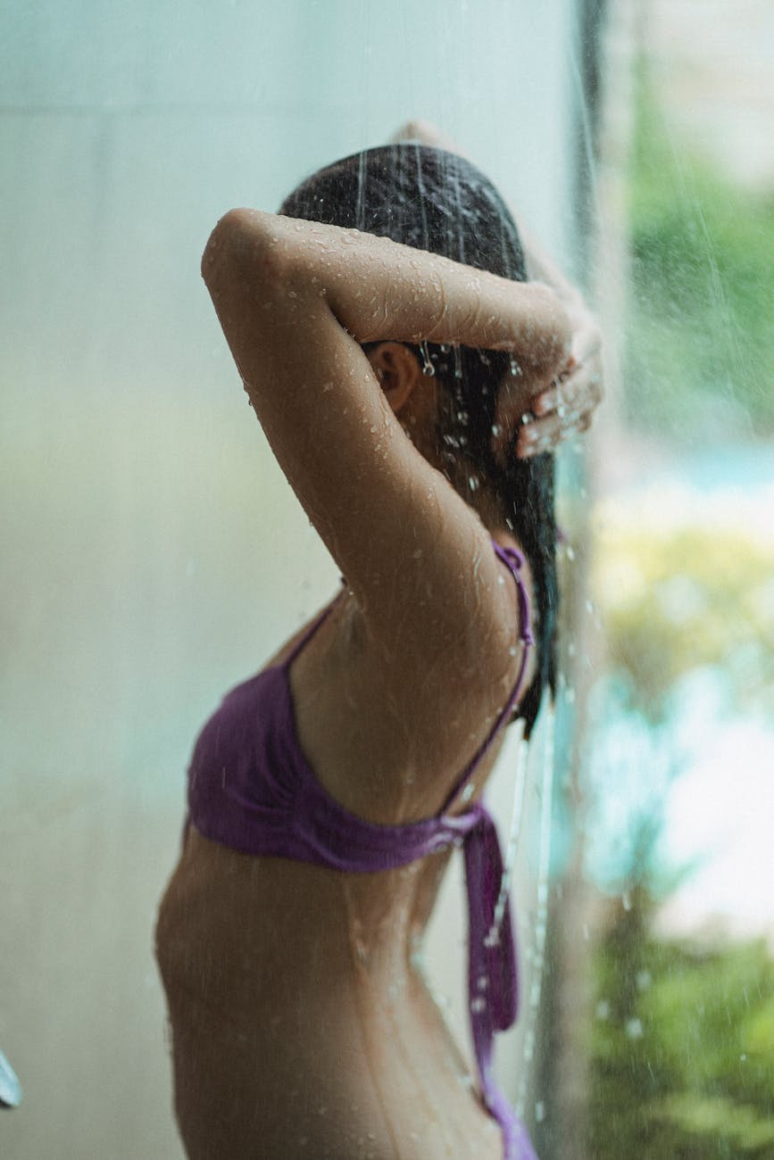 young woman in swimwear standing under water stream